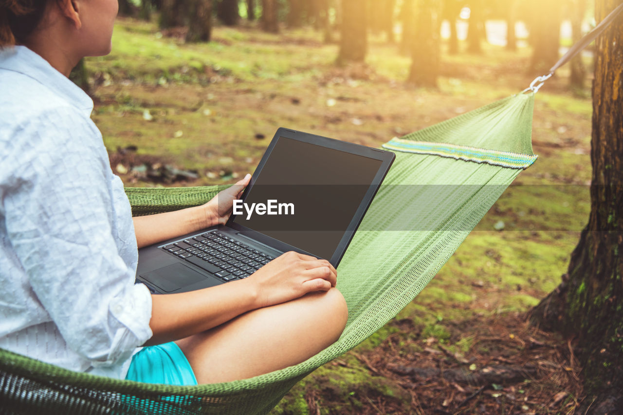 Midsection of woman using laptop while sitting on hammock