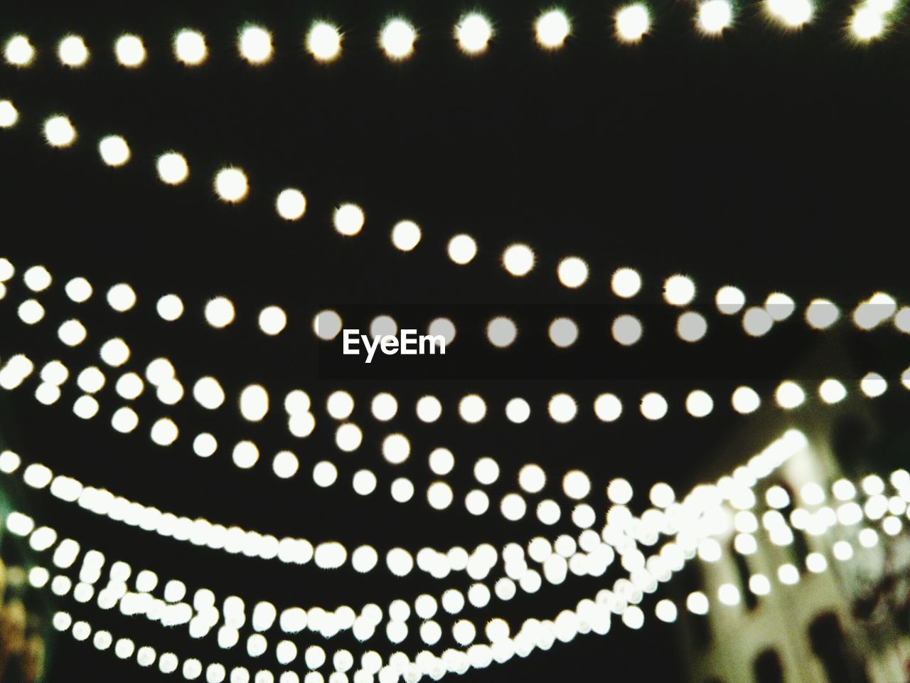 Defocused image of illuminated string lights against sky at night