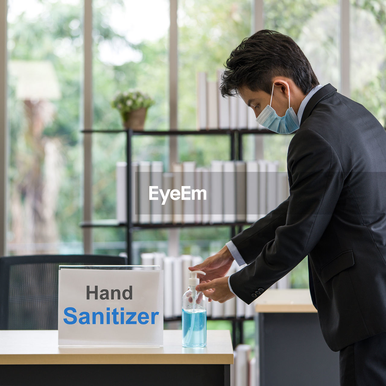 Side view of a young man with mask pouring sanitizer in hand