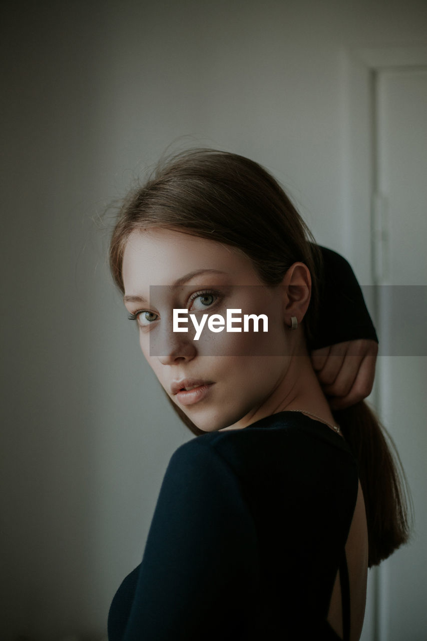 Portrait of beautiful young woman standing against wall at home