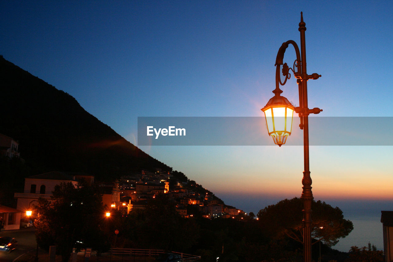 ILLUMINATED STREET LIGHT BY BUILDING AGAINST SKY AT NIGHT