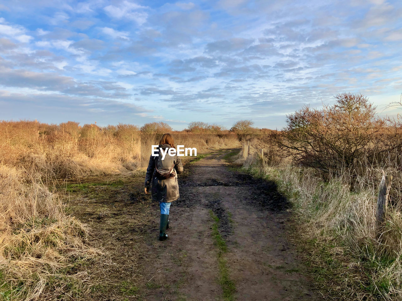 Rear view of woman walking on field against sky