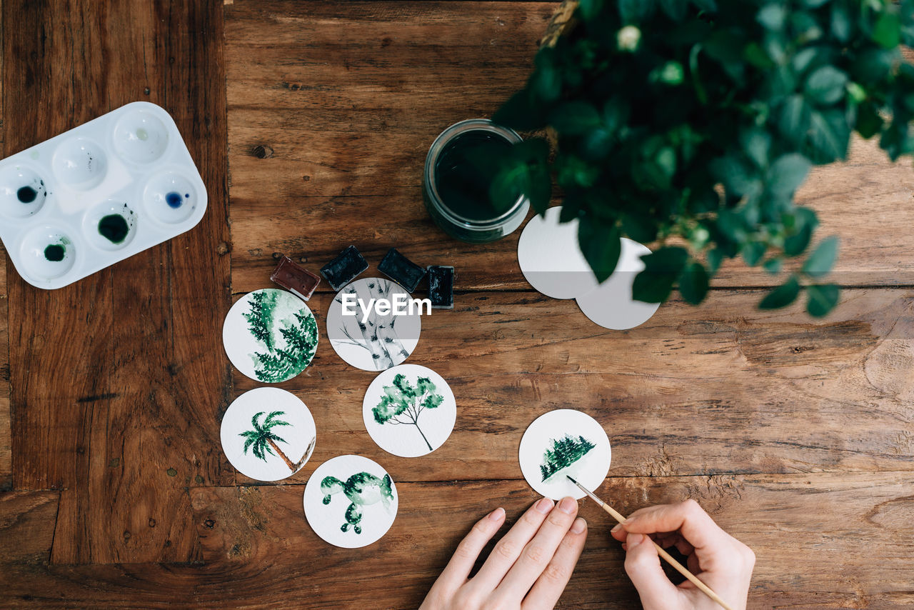 Cropped hands of woman doing aquarelle at wooden table