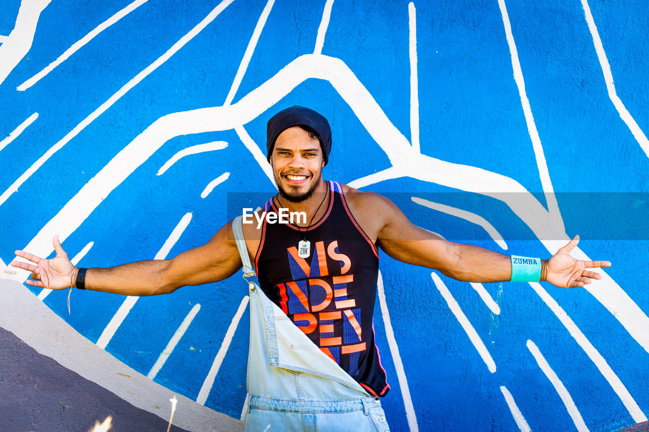 PORTRAIT OF HAPPY YOUNG MAN WITH ARMS RAISED