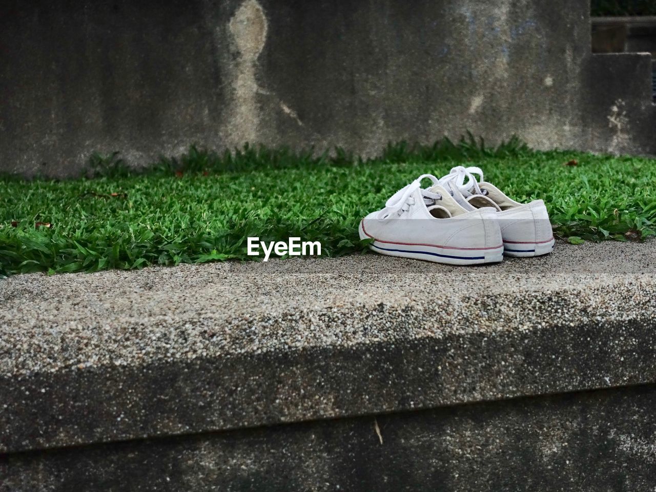 CLOSE-UP OF SHOES ON FOOTPATH AGAINST WALL