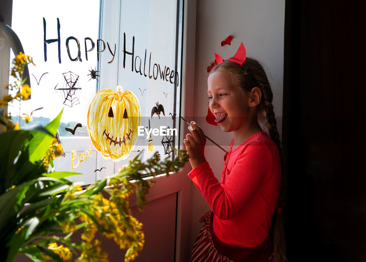 Child painting pumpkin window preparing celebrate halloween kid draws decorates room with paper bats