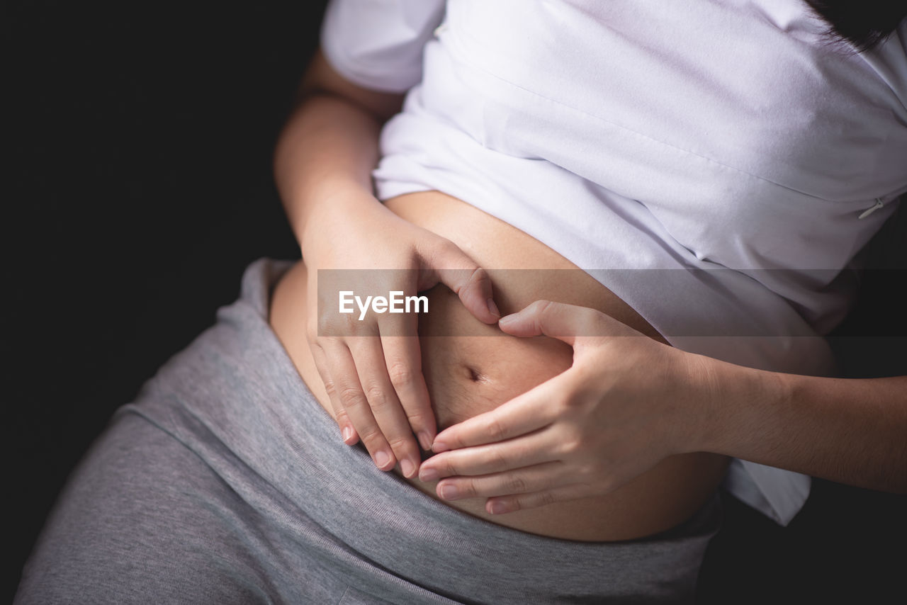 Midsection of woman making heart shape on pregnant belly