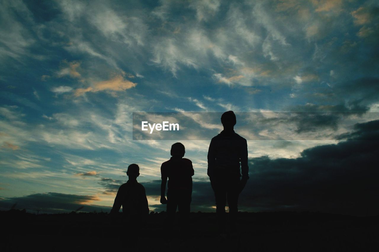 Silhouette of people standing on landscape against cloudy sky