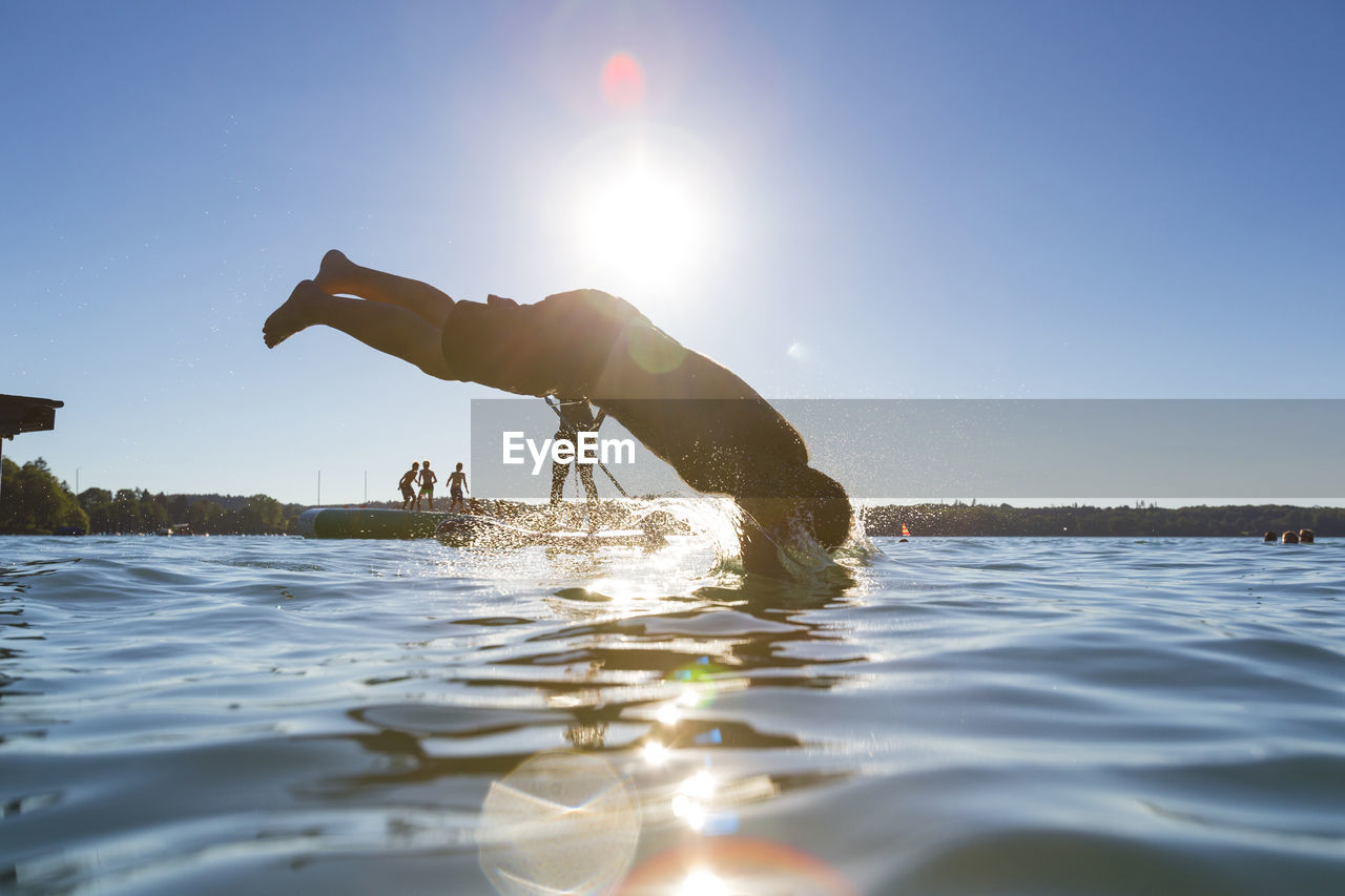Side view of man diving into lake against clear blue sky on sunny day