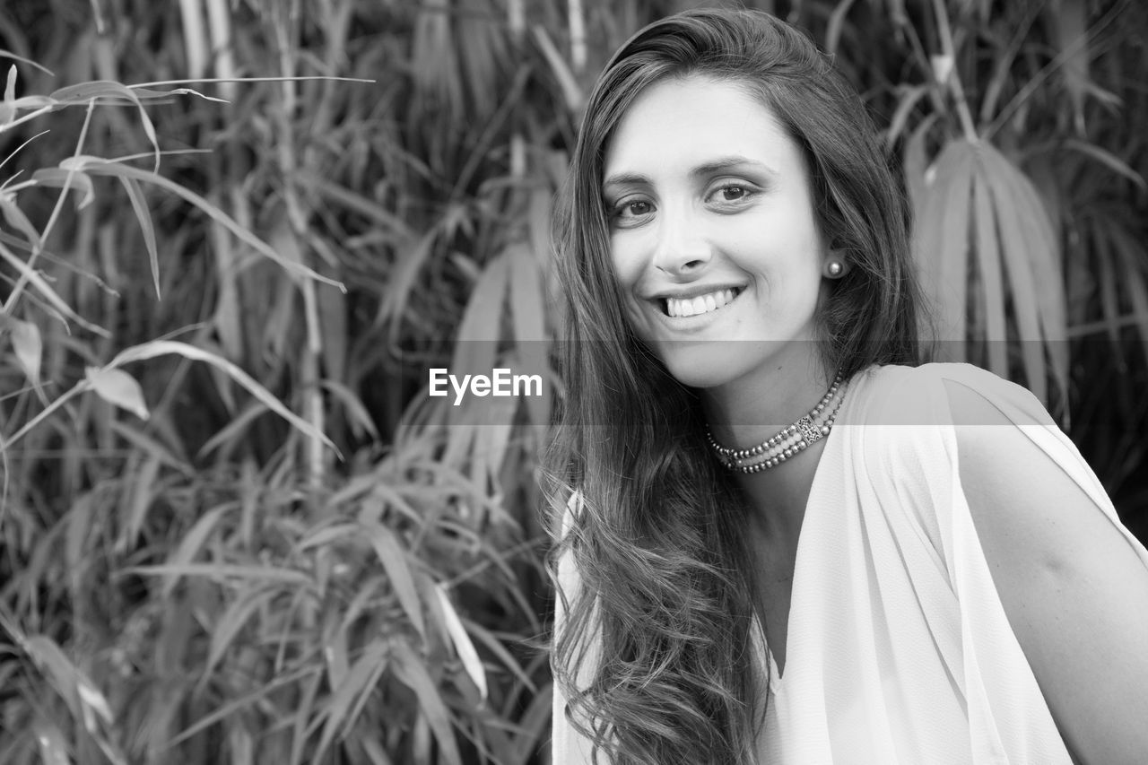 Portrait of smiling young woman standing against trees