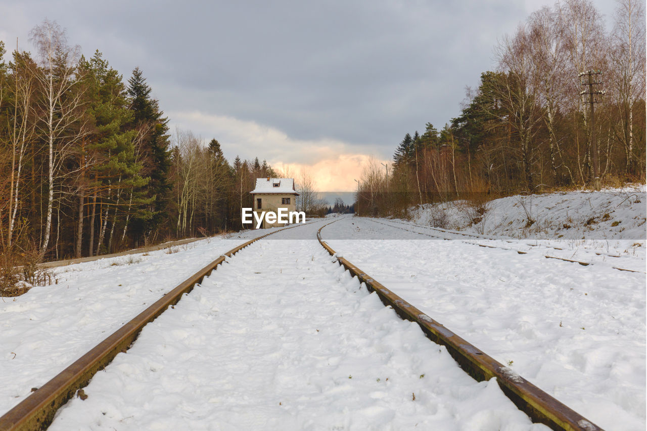 Snow covered railroad tracks by trees against sky