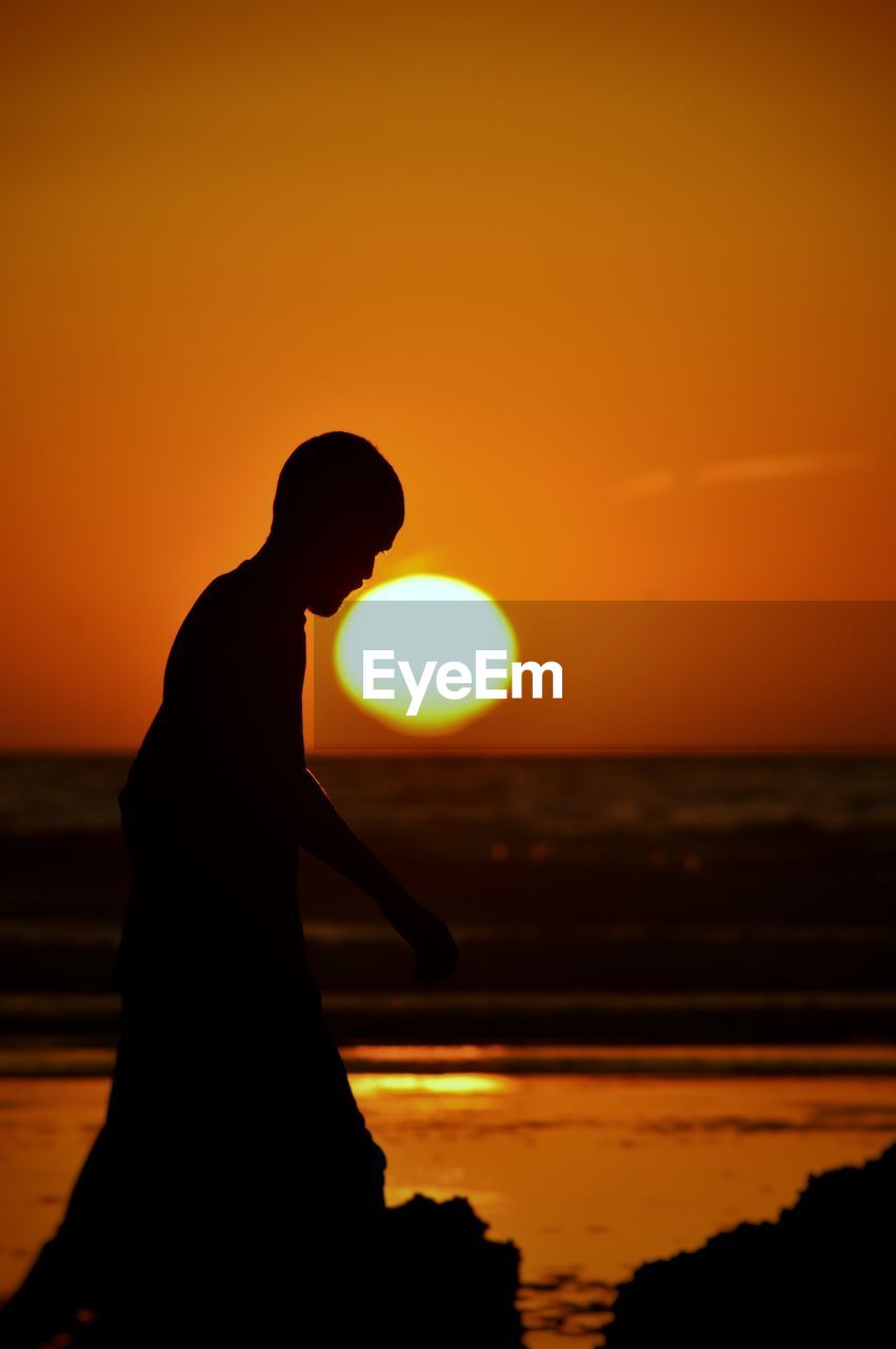 Silhouette men standing by sea against orange sky