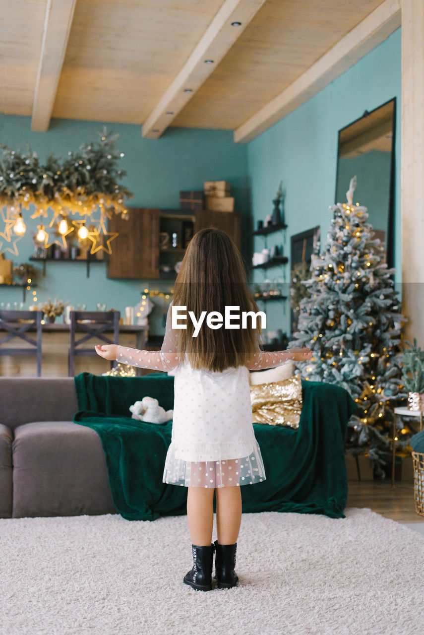 A girl with long hair stands with her back to the living room decorated for christmas
