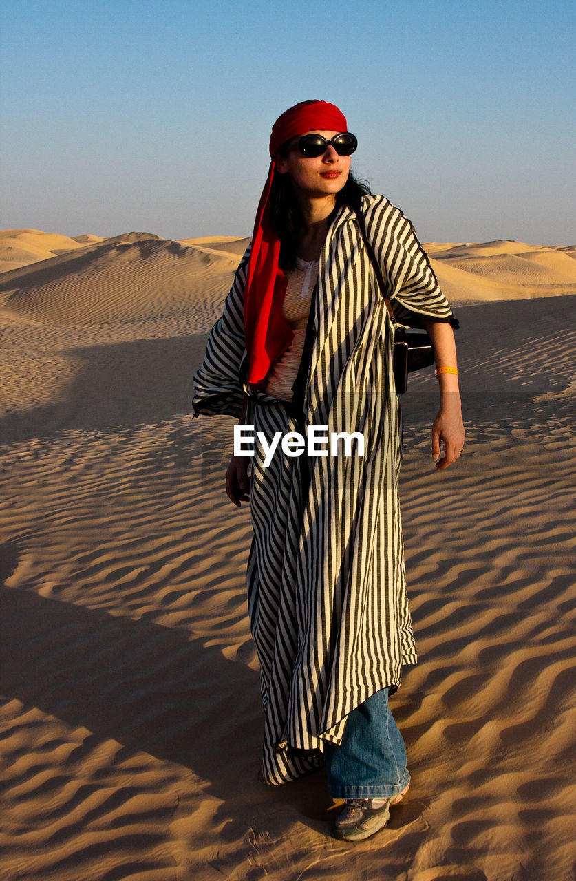 Young woman wearing sunglasses on sand in desert against sky