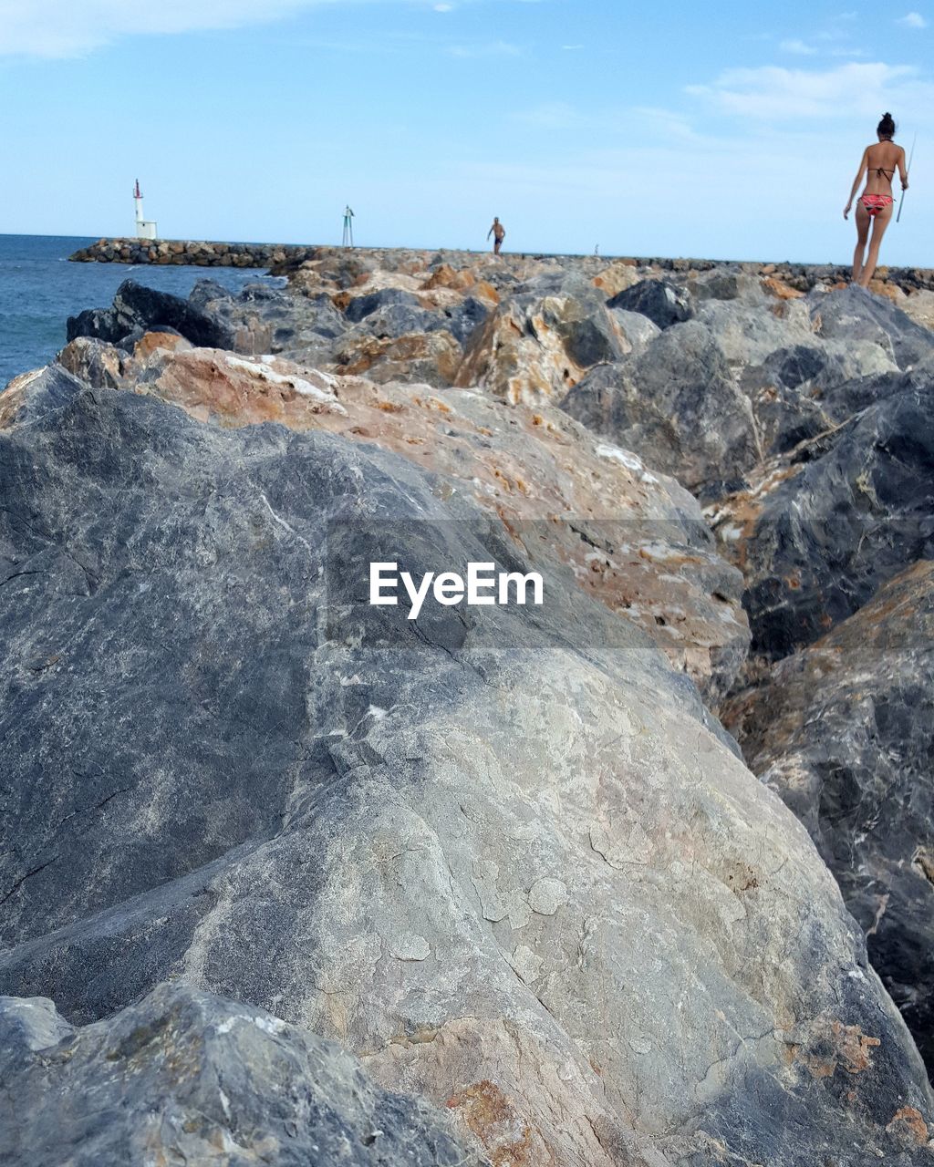 REAR VIEW OF MAN STANDING ON ROCK BY SEA