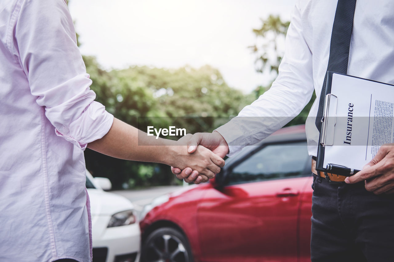 Midsection of man handshaking with insurance agent at parking lot