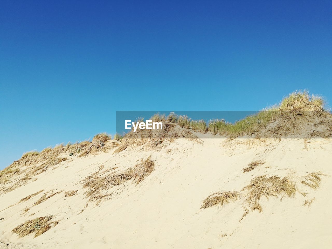LOW ANGLE VIEW OF SAND AGAINST CLEAR BLUE SKY
