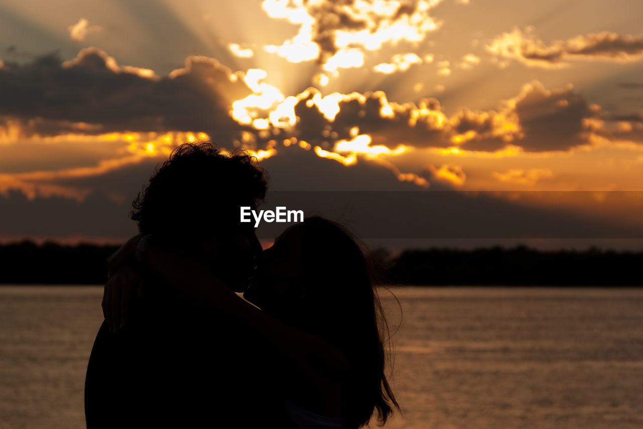 Silhouette couple kissing against sea at sunset