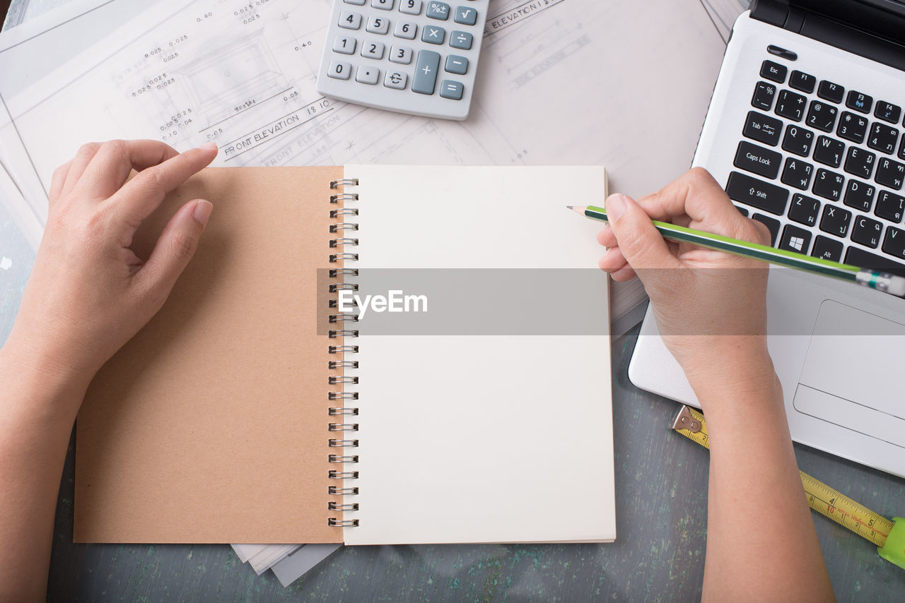 Cropped hands of woman writing on book at desk