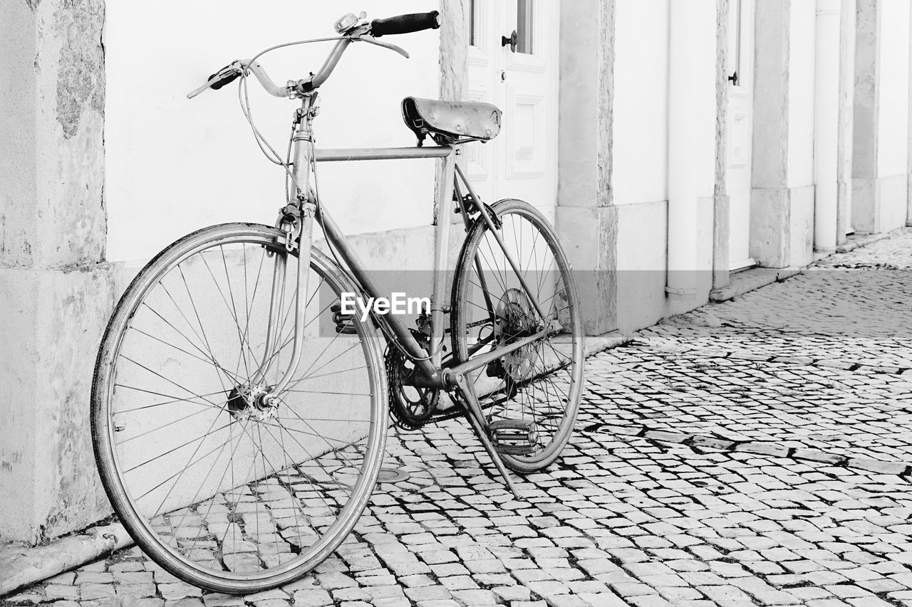 bicycle, transportation, land vehicle, mode of transportation, architecture, vehicle, black and white, city, white, no people, street, road bicycle, monochrome, wall - building feature, built structure, monochrome photography, building exterior, footpath, wheel, day, sidewalk, outdoors, sports equipment, parking, cobblestone, leaning, bicycle wheel, iron, travel, old, nature