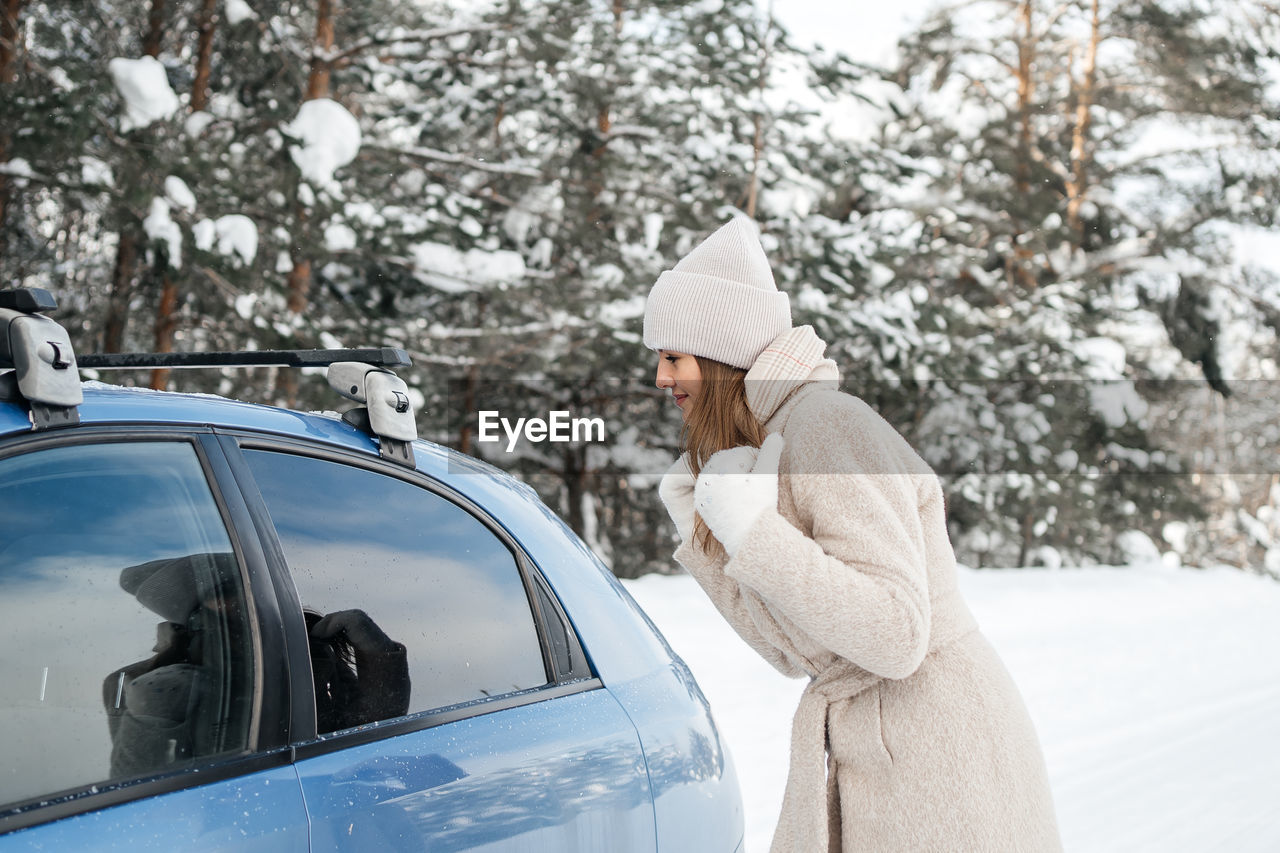 Girl in the winter forest pretends to be reflected in the window of the car