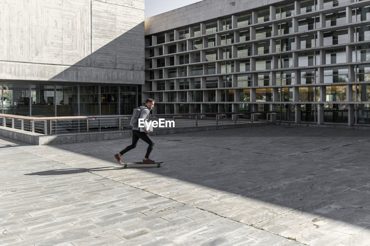 Mature male commuter skateboarding against building