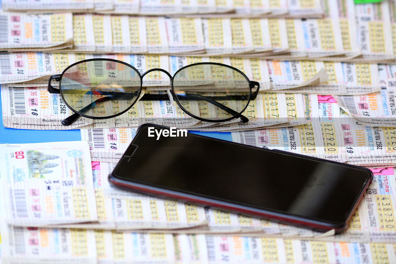 Close-up of mobile phone with eyewear over newspaper on table