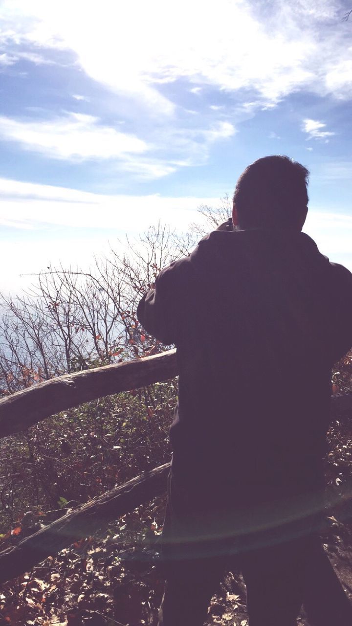 Rear view of man standing by railing against sky