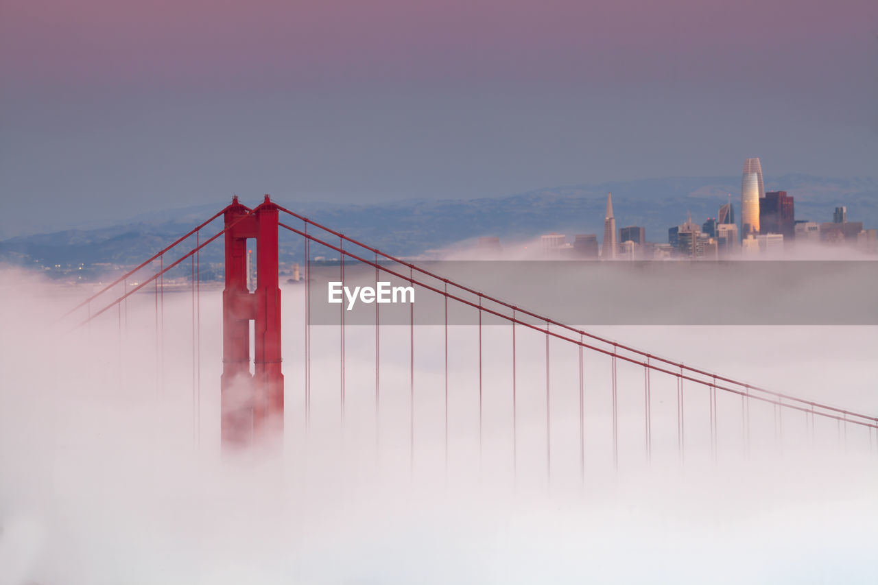 architecture, built structure, bridge, fog, suspension bridge, transportation, sky, travel destinations, city, nature, water, travel, building exterior, engineering, cloud, landscape, tourism, cityscape, red, environment, beauty in nature, sea, morning, outdoors, urban skyline, twilight, scenics - nature, dusk, long exposure, copy space, winter, bay, city life, building, business finance and industry, atmospheric mood, bay of water, panoramic, dramatic sky, tranquility, cable-stayed bridge, motion, mountain, illuminated, mode of transportation, skyscraper