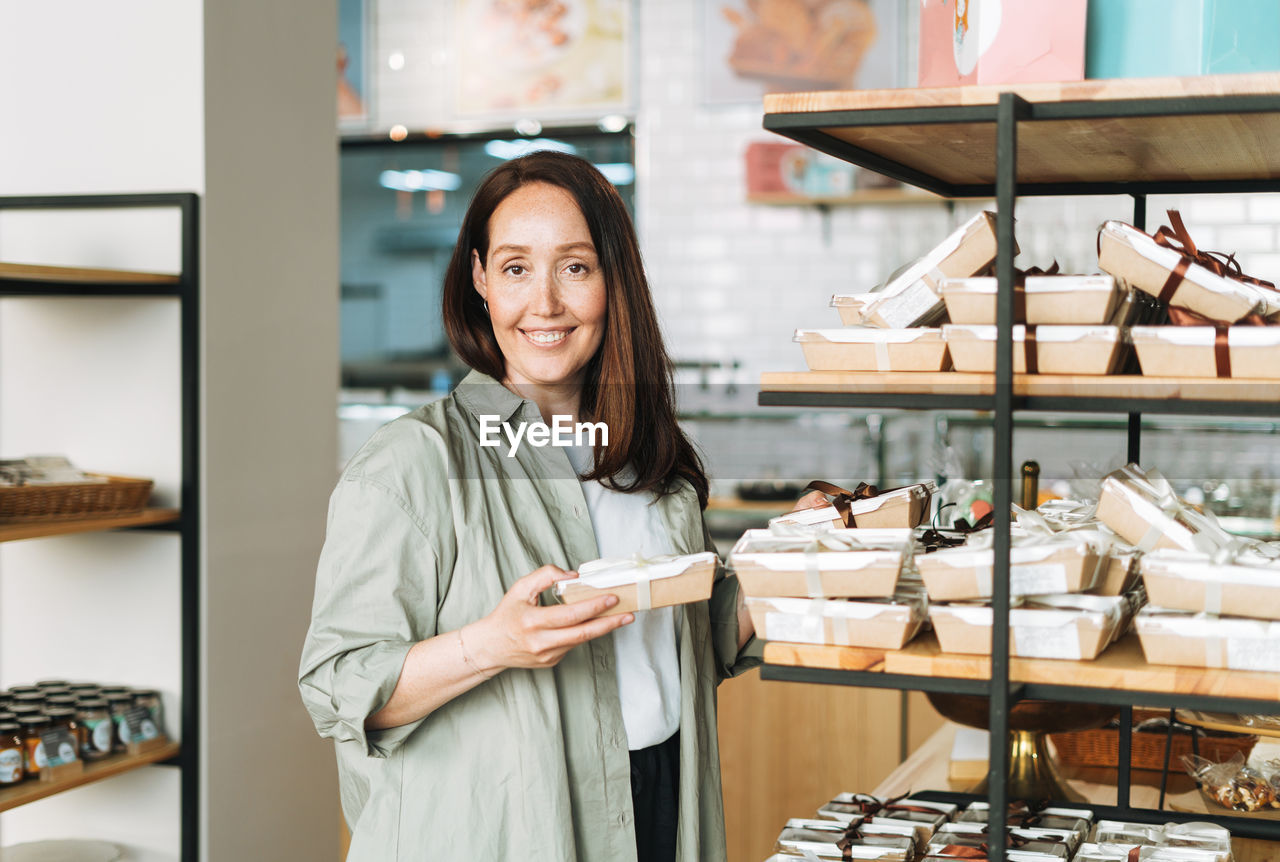 Adult smiling brunette woman forty years choosing sweets in cafe, woman having  in confectionery