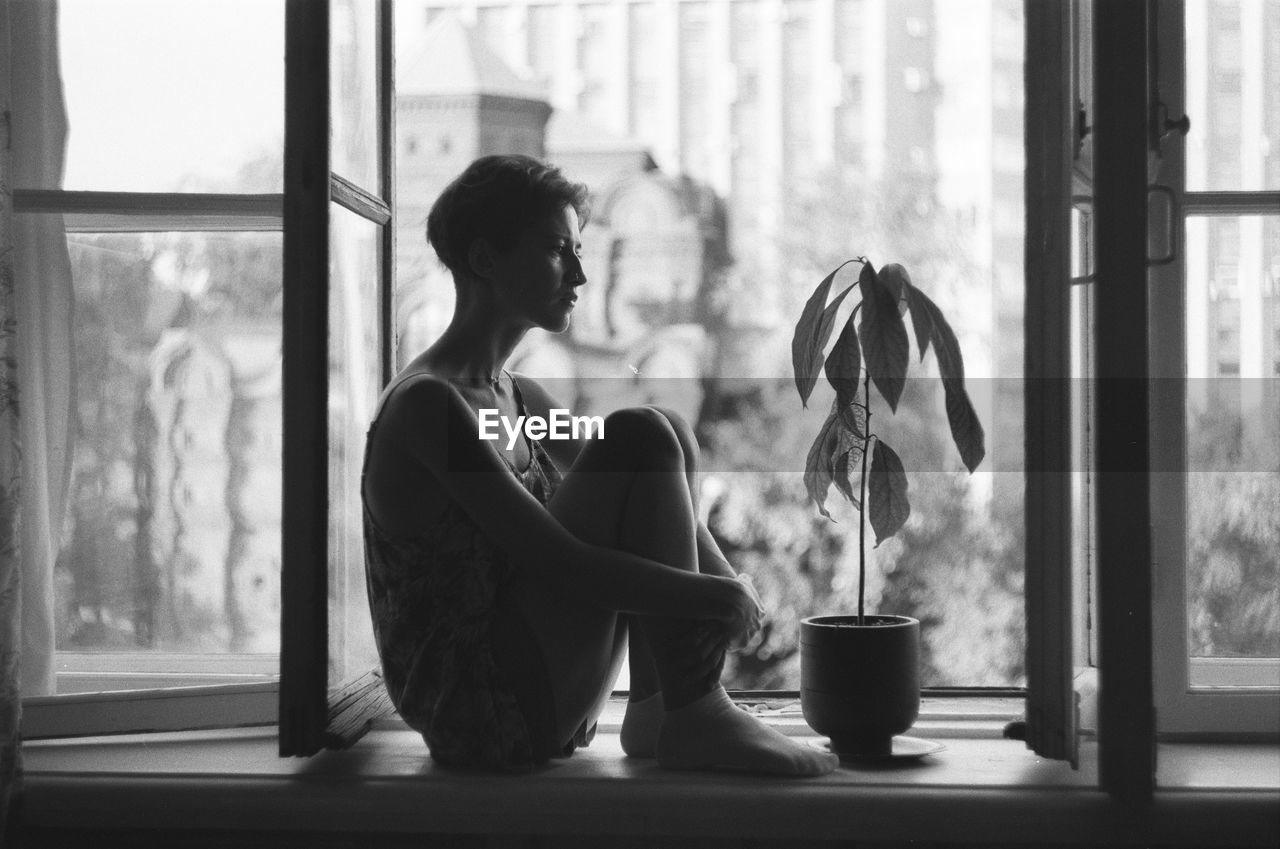 Side view of woman sitting by window at home