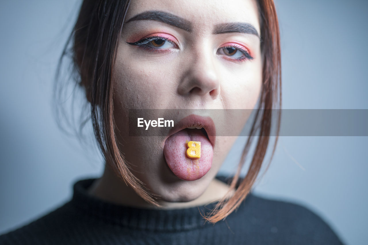 Portrait of woman licking candy against gray background