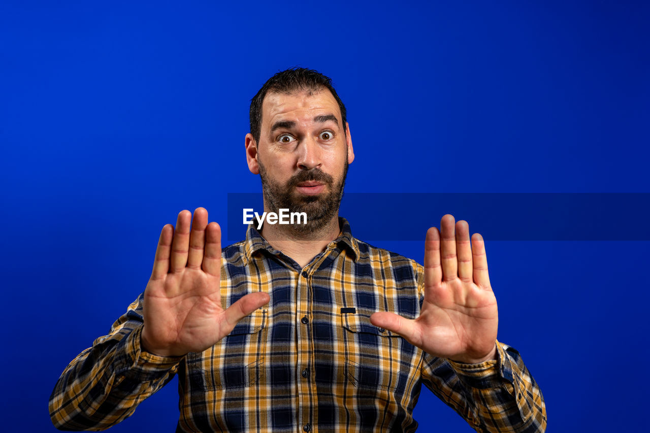 PORTRAIT OF MAN WITH ARMS OUTSTRETCHED AGAINST BLUE BACKGROUND