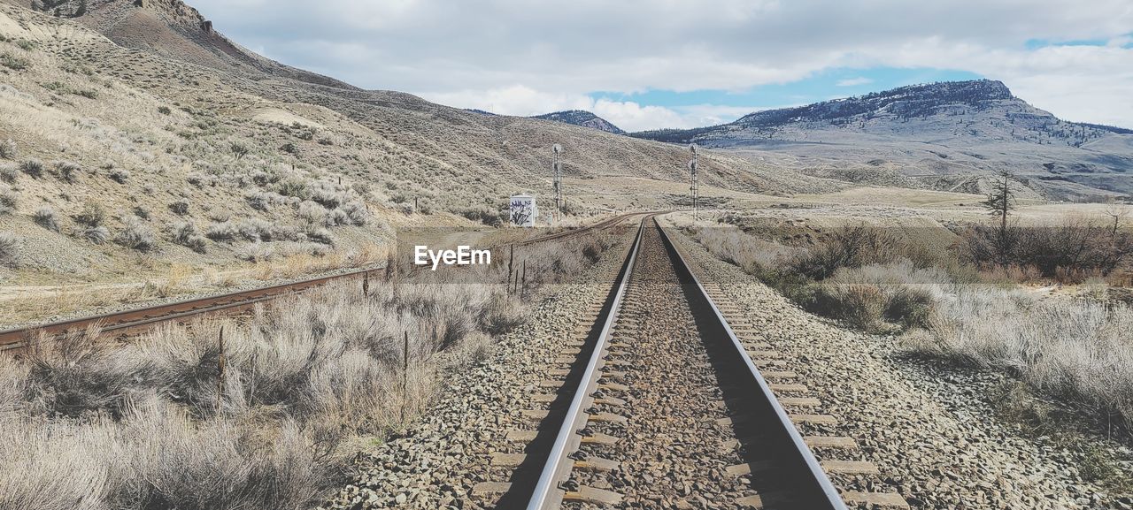 Railroad track leading towards mountain range against sky