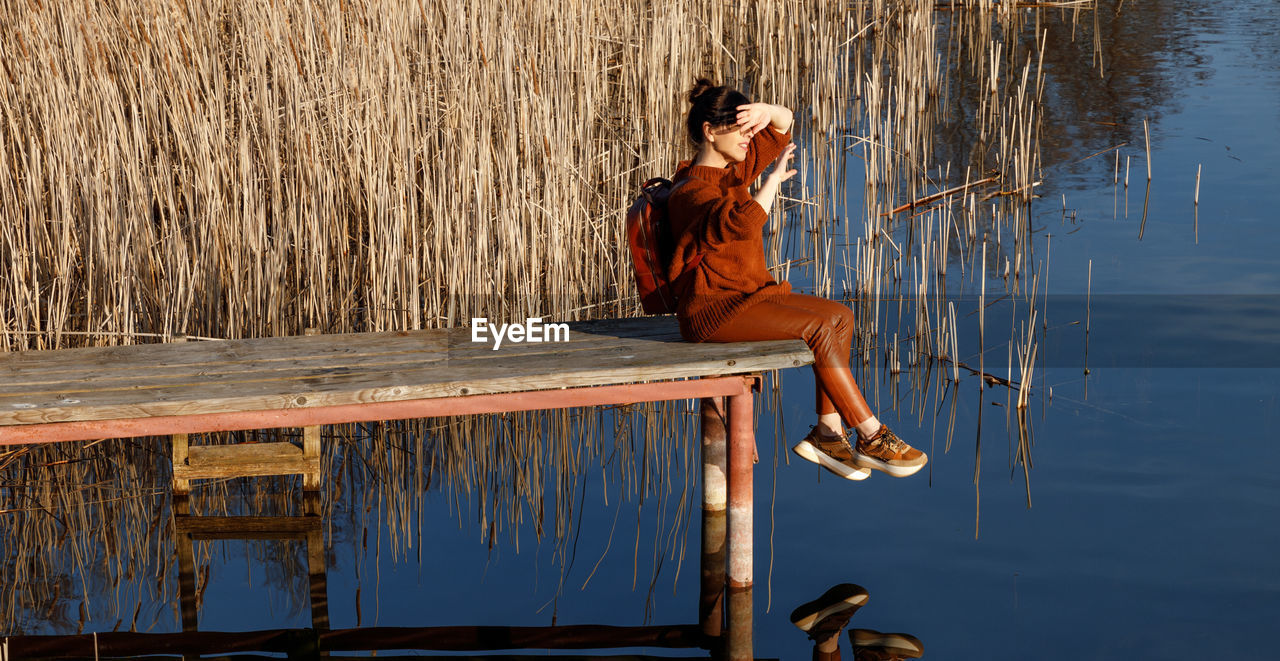Side view of woman sitting on pier over lake