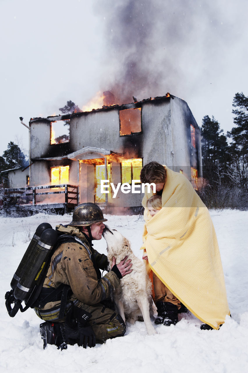 Fireman with rescued people and dog in front of burning house