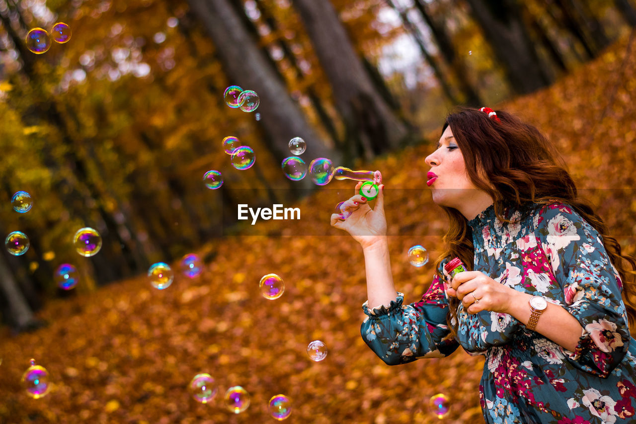 Mid adult woman blowing bubbles in forest during autumn