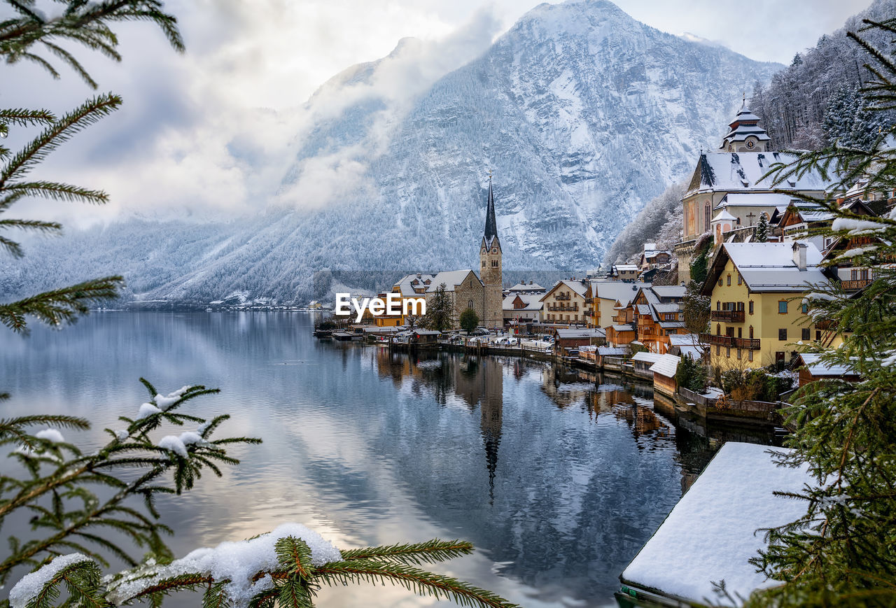 Scenic view of lake by buildings and snowcapped mountains during winter