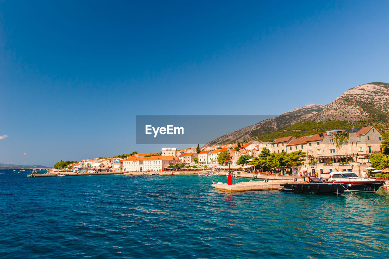 Scenic view of sea and buildings against clear blue sky