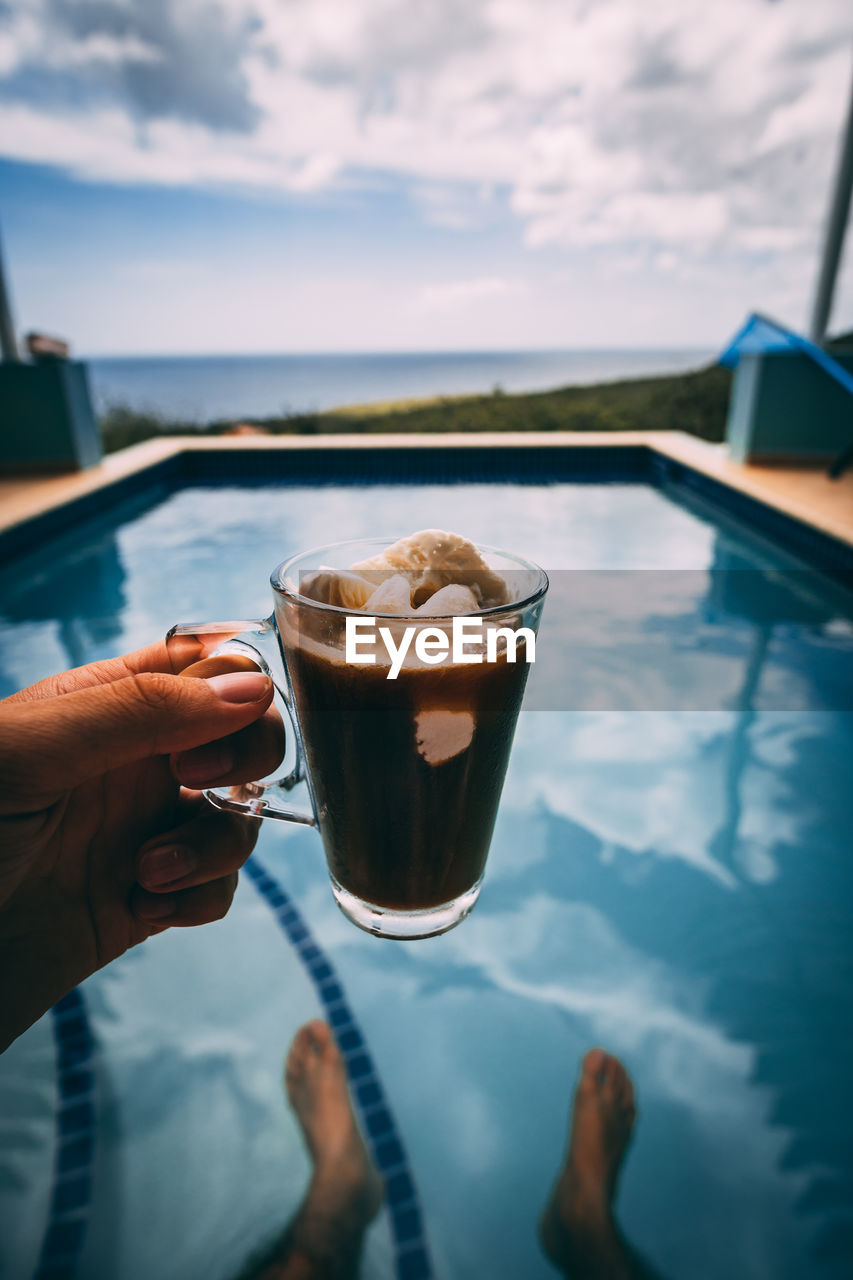 Cropped hand of woman holding drink by swimming pool