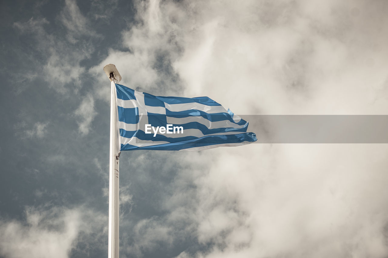 Waving greek flag against a blue sky with clouds. muted colors.