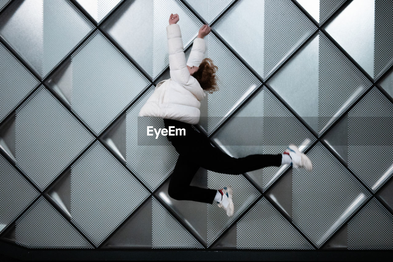 Side view of young woman in mid-air jumping against pattern wall