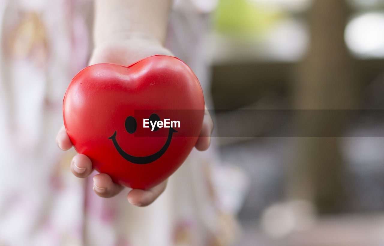 Close-up of hand holding red smiley heart shape toy