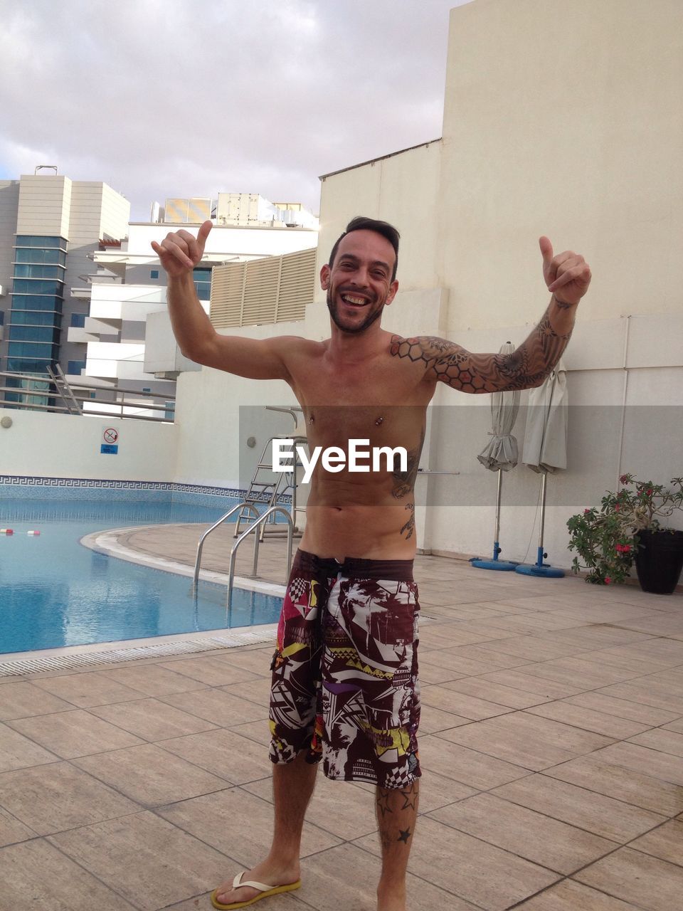 Portrait of smiling man showing shaka sign at poolside