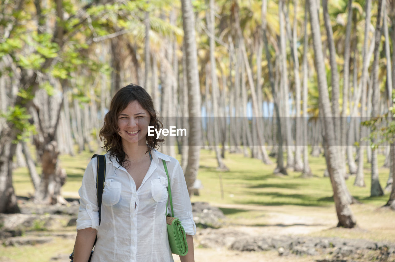 Portrait of smiling woman standing against palm trees on field