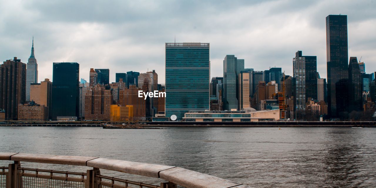 Modern buildings by river against sky in city