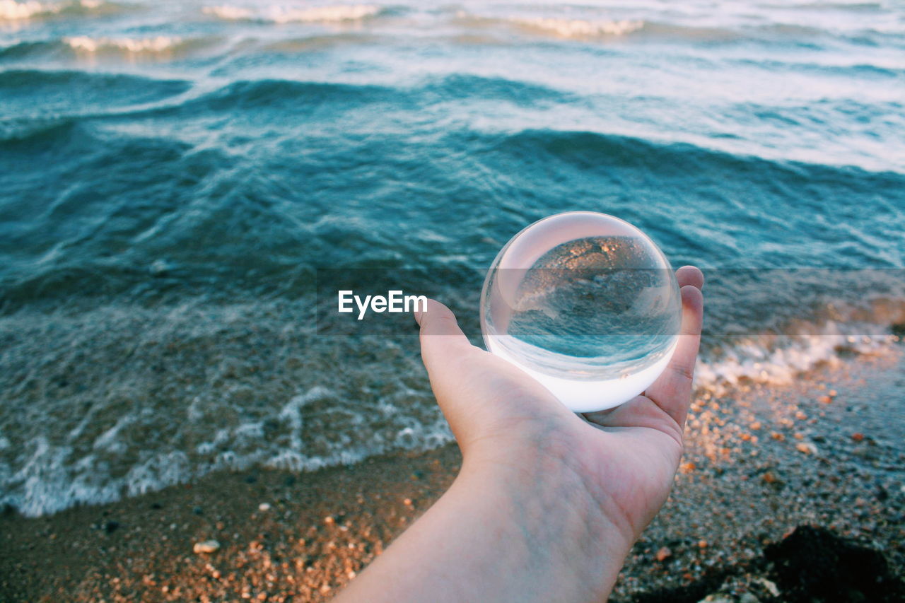 Cropped hand holding crystal ball against sea