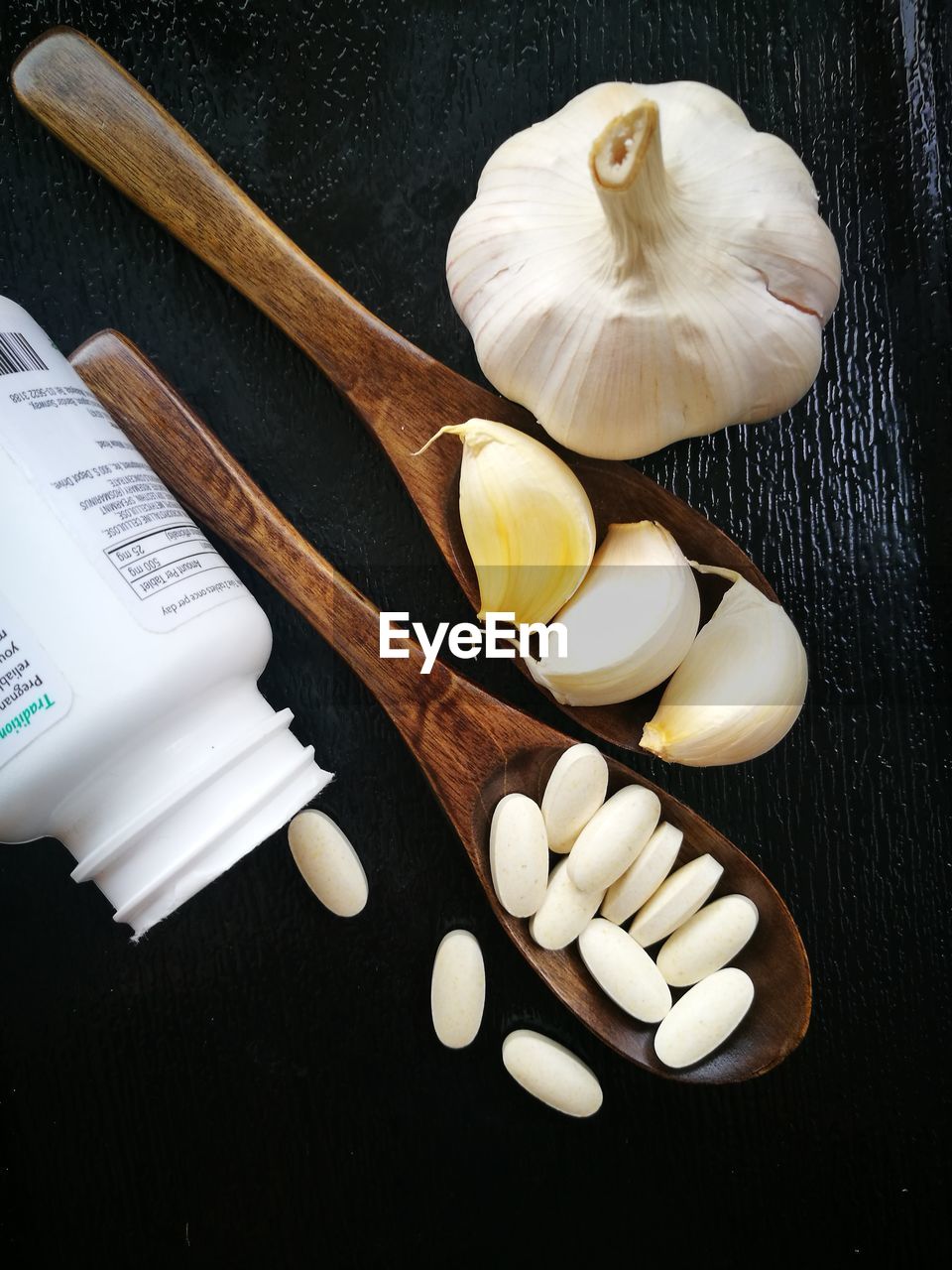 Directly above shot of pills and garlic in wooden spoons on table