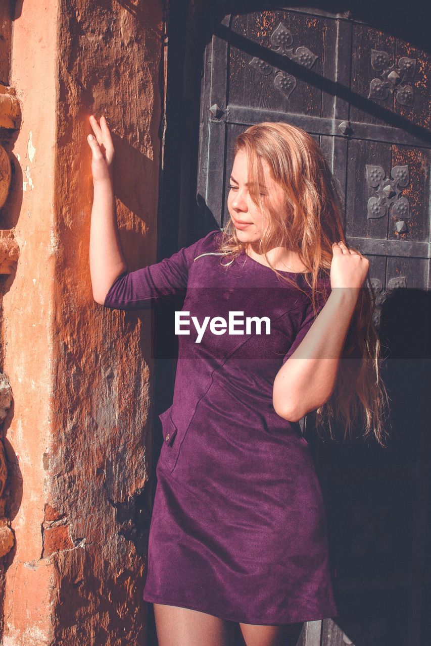 YOUNG WOMAN STANDING IN FRONT OF WALL WITH ARMS RAISED