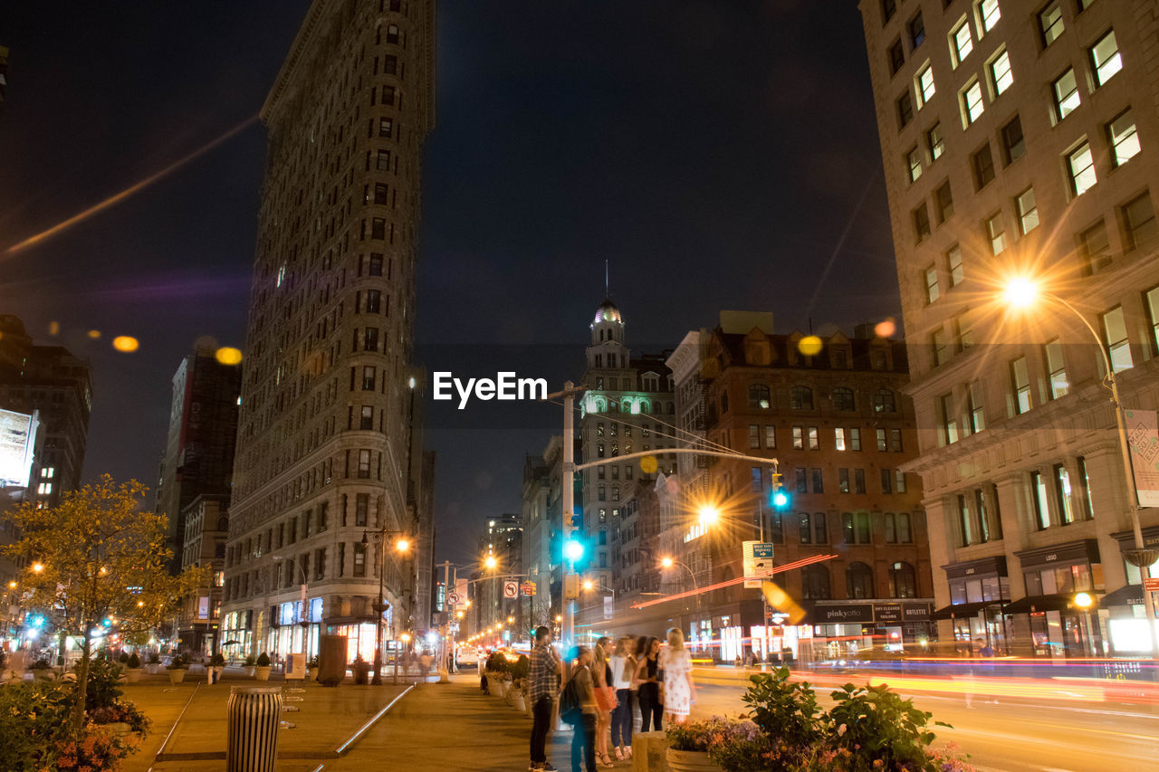 People standing by flatiron building at night